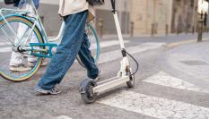 Persona caminando con un patinete eléctrico por un paso de peatones en la ciudad.