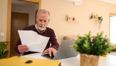Hombre mayor revisando una factura frente al ordenador en casa.