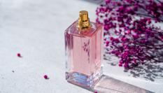 Un frasco de perfume de color rosa junto a unas flores