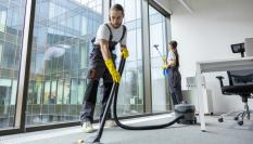 Trabajadores limpiando unas oficinas con aspiradora y productos de limpieza.