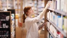 Imagen de archivo de una farmacéutica revisando estantes de medicamentos.