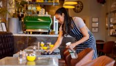 Imagen de una camarera limpiando una mesa tras un servicio.
