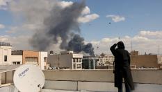 Una mujer, desde una terraza, ve el humo de los bombardeos en Teheran
