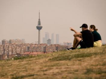 Unos madrileños miran al cielo este sábado teñido de gris por los incendios forestales.