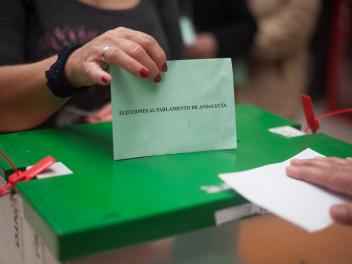 Urna de las elecciones al Parlamento de Andalucía con una mano votando.