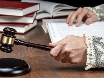 Primer plano de las manos del juez golpeando el mazo, con la toga con puños de encaje y los libros de derecho sobre el escritorio en la sala del tribunal, en una imagen de archivo.
