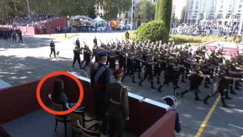 Está Letizia sentada y de fondo una señora hace esto: también se ve lo que hace la reina