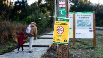 Cartel de alerta por peste porcina africana en un sendero de Collserola, con dos personas caminando al fondo.
