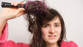 Una mujer trata de peinarse el pelo mojado y enredado. Cuidado del cabello en casa, pérdida de cabello y sección