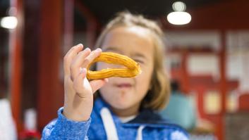 Chica rubia comiendo churros con chocolate sentada en una mesa de cafetería, jugando con uno. Invierno, desayuno, merienda, azúcar y felicidad.