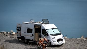 Dos viajeros se sientan fuera de su autocaravana estacionada en la orilla un lago