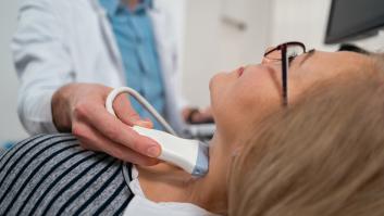 Primer plano de un médico caucásico irreconocible, un endocrinólogo, que realiza una ecografía de la glándula tiroides a una paciente mayor en la clínica médica.