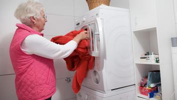 Una señora de 75 años metiendo su ropa en la lavadora del baño.