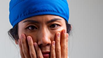 Trabajadora de la salud, adulto de mediana edad, seria, con exceso de trabajo y estresada, mirando a la cámara sobre un fondo gris