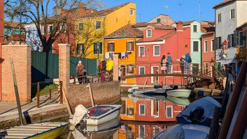 La gente caminando por una pasarela sobre el canal con barcos amarrados en Burano