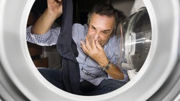 Un hombre cogiendo un calcetín que huele mal en la lavadora