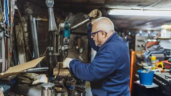 Un hombre anciano usando el taladro en su taller con gafas y guantes de protección