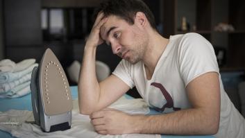 Un joven plancha su ropa en casa, con el interior de la vivienda de fondo.