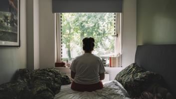 Mujer de espaldas en su habitación, viendo hacia la ventana.