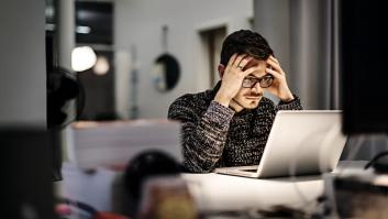 Un joven hombre de negocios, con gafas y aspecto informal, sentado frente a su portátil, con la cabeza entre las manos