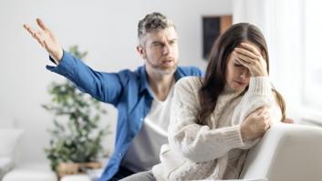 Un marido gritando a su pareja en el sofá de casa, quien lo ignora y se lleva las manos a la cabeza con frustración.