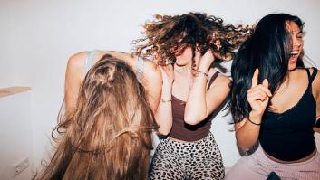 Three women share a lively moment, flipping hair and laughing as they dance in a bright, minimal room. A candid scene of friendship, energy, and carefree youth. Part of a series with video