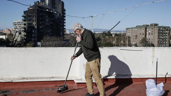 Un vecino de Valencia limpia los restos de ceniza de la azotea, con el edificio incendiado al fondo.