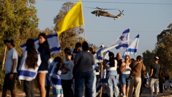 Un helicóptero vuela mientras la gente se reúne, en Reim (Israel), en la base donde se espera que lleguen los rehenes de Israel, este lunes.