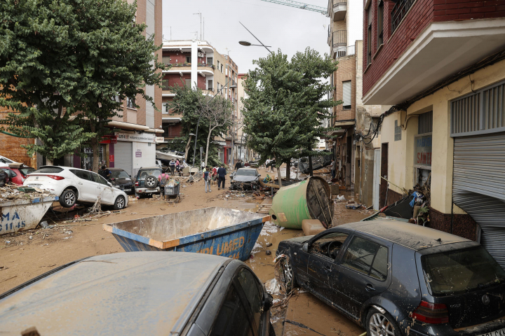 Unas personas caminan por una calle cubierta de lodo y llena de coches amontonados tras las intensas lluvias por la fuerte dana que afecta especialmente el sur y el este de la península ibérica, este miércoles en Valencia.