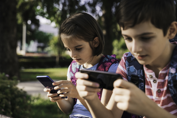 Un niño y una niña con un móvil cada uno mientras están en el parque.