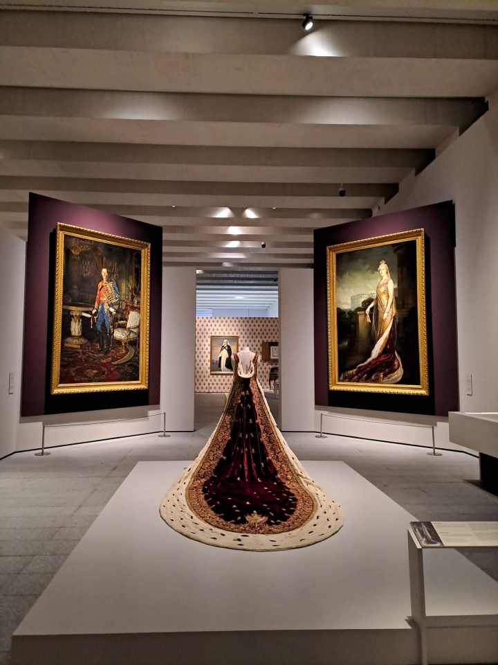 Retratos de Alfonso XIII y Victoria Eugenia y el manto de terciopelo y armiño de Ena en la exposición de la reina Victoria Eugenia