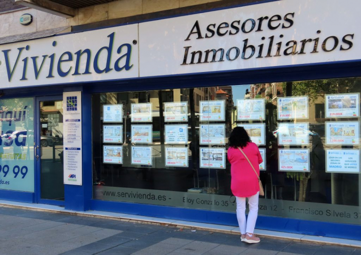 Mujer mirando anuncios de venta y alquiler en el escaparate de una inmobiliaria.