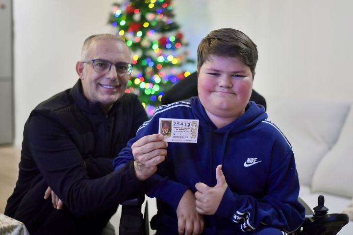 Álvaro, un niño de 13 años que padece laminopatía congénita, posa junto a su padre, y el quinto premio en la Lotería de Navidad, elegido por su fecha de nacimiento