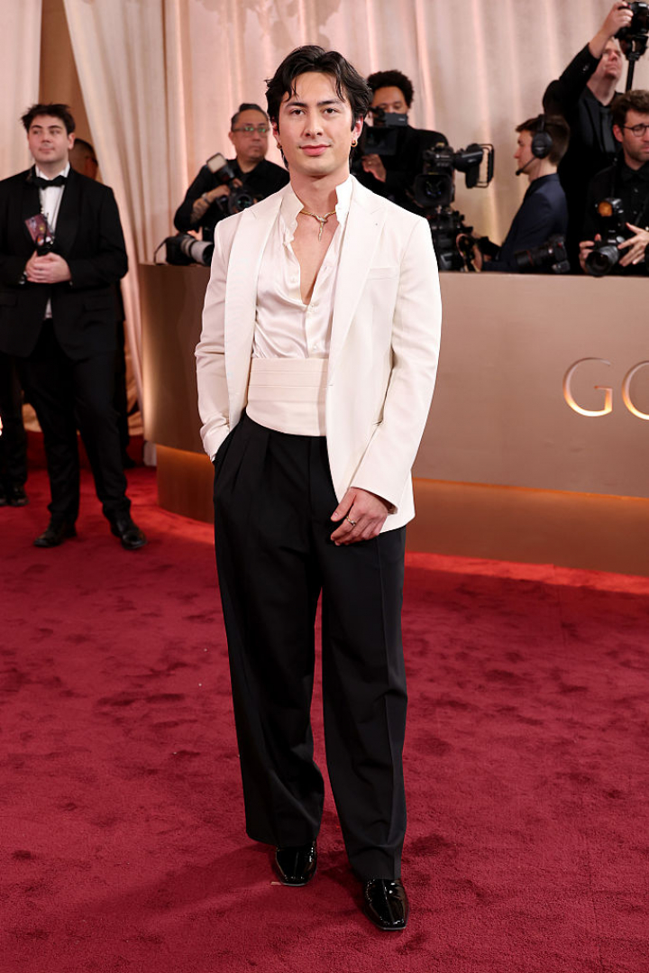 alt="alt="La estrella de la serie revelación de la Navidad, Heated Rivalry, apostó por una camisa satinada combinada con un fajín y una americana en color blanco. Williams la llevaba abierta para dejar ver el collar dorado en forma de serpiente.""