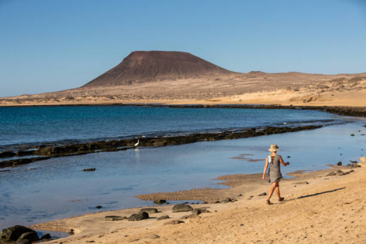 alt="alt="A woman walks along the sand as gentle waves break on exposed volcanic rock at low tide on 23rd November 2020, on Playa Del Salado on La Graciosa island off Lanzarote, Spain. (Photo by Jonathan Perugia/In Pictures via Getty Images).""