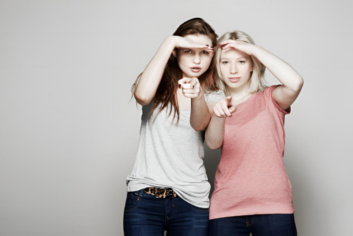 alt="alt="Dos chicas jóvenes señalando y mirando a cámara""