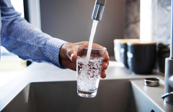 La mano de un hombre sirviéndose un vaso de agua del grifo en el fregadero de la cocina