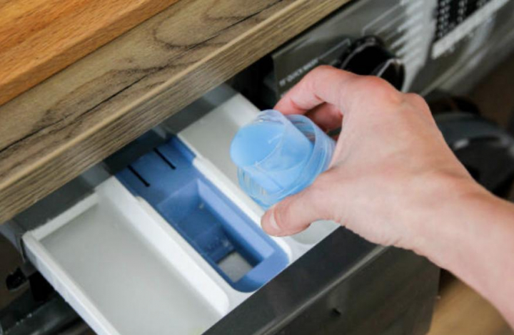 Una persona echando detergente en el cajón de la lavadora