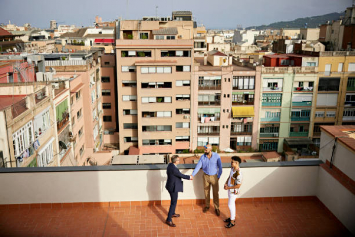 alt="alt="High angle full length view of mature salesman shaking hands with mid adult gay couple as they stand on outdoor balcony with view of residential district.""