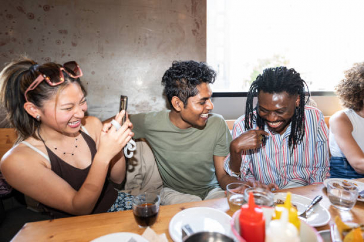 alt="alt="A group of people are sitting around a table, laughing and taking pictures. Scene is lighthearted and fun""