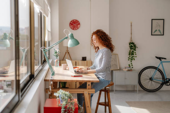 alt="alt="Woman sitting on a desk using a laptop computer while working from home. Business, freelance and home office concept.""