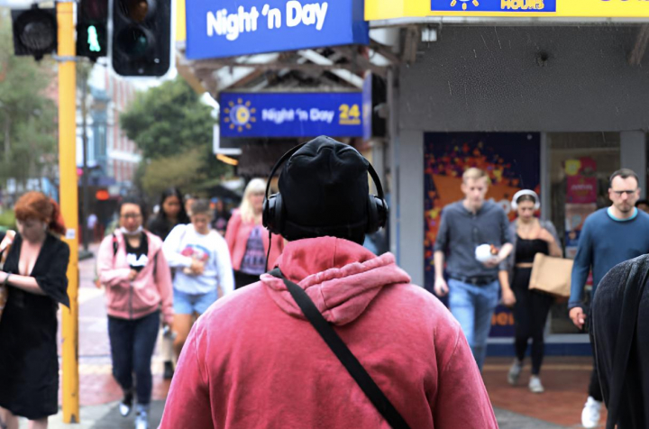 alt="alt="Un joven con auriculares caminando por una calle llena de gente""