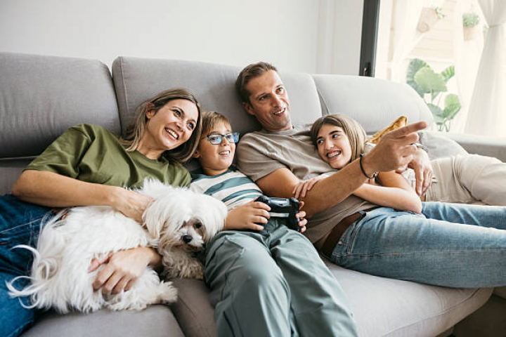 alt="alt="Happy family spending time together on the sofa, watching tv and enjoying their pet""