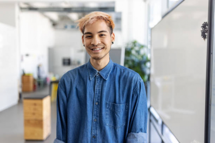 alt="alt="Portrait of young businessman with colored hair. Man standing in office looking at camera and smiling.""