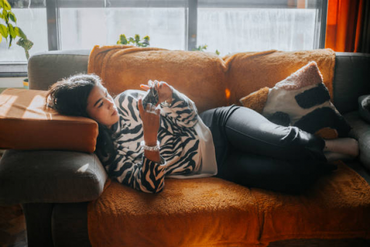 alt="alt="young female teenager using cell phone at home while is sitting on desktop at home""