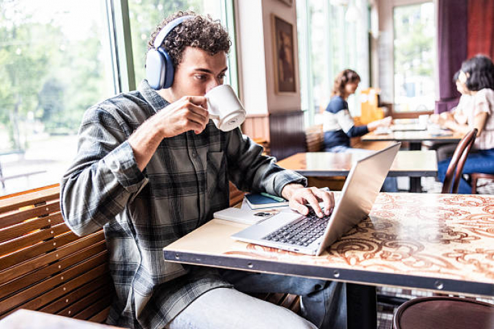 alt="alt="Young man wearing headphones and working on laptop in coffeeshop""