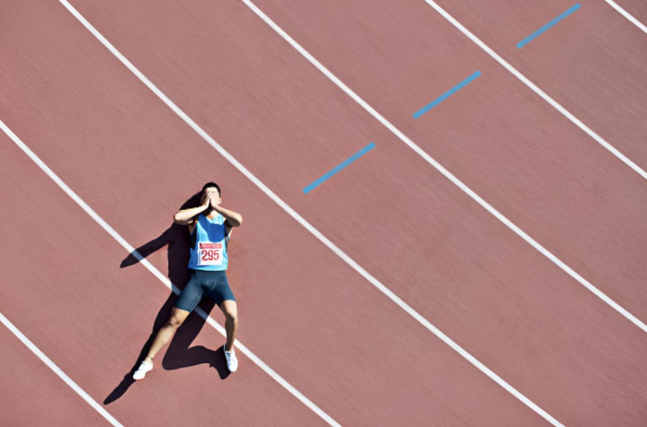 Un atleta tumbado bocarriba en mitad de la pista con las manos en la cara