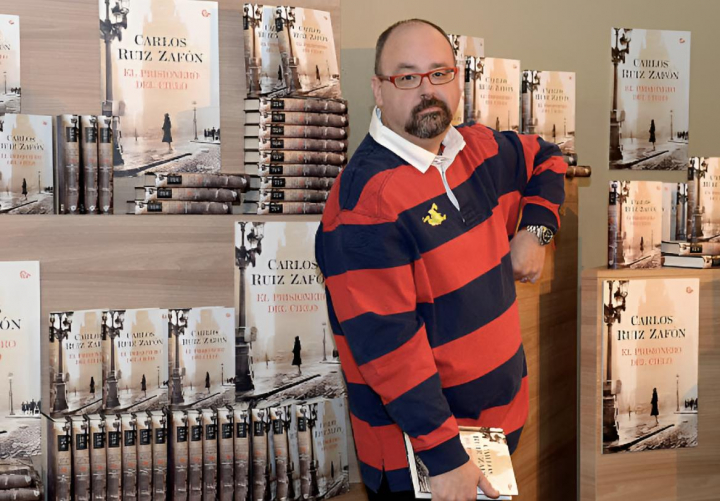 alt="alt="El escritro Carlos Ruiz Zafón posando con sus libros de fondo""