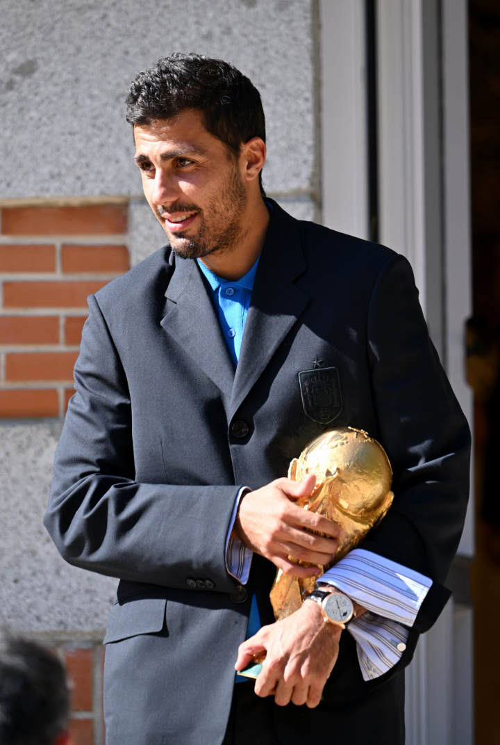 Rodri, con el traje y el polo azul, portando la copa del mundo