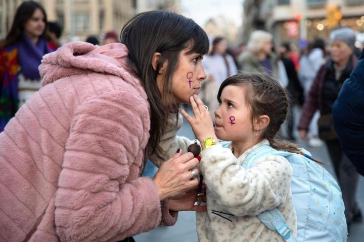 Una niña le pinta la cara a una mujer durante la manifestación del 8 de marzo de 2023 en Barcelona.